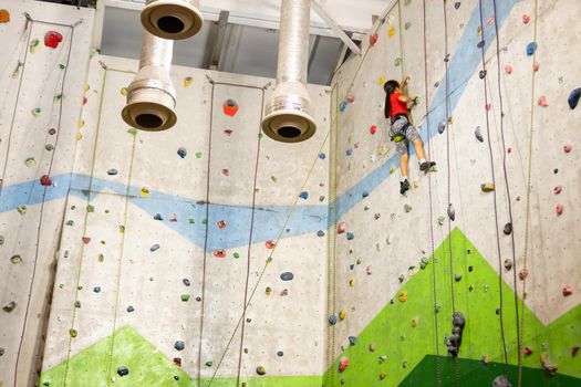 Sporty little girl climbing artificial boulder on practical wall in gym