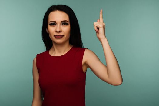 Closeup of serious strict young woman wears red dress looks stressed and pointing up with finger isolated over blue background - Image