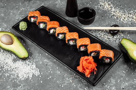 A set of sushi rolls Philadelphia with red fish, cream cheese and black rise lies in a plate boat. Sushi rolls on a gray background.