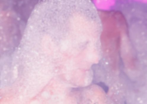 Head and face of a guy in soapy foam with bubbles at a foam party, close-up, blurred.