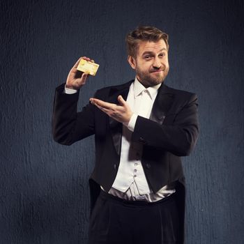 Positive man in a tailcoat demonstrates shows a credit card. - image