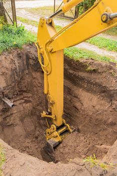 Hydraulic excavator piston digs deep pit in industrial area on construction site.