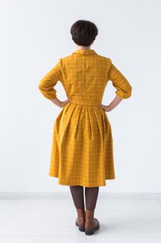 clothing, designer, people concept - back view of attractive woman in a yellow dress posing on white room