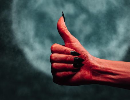 Red demon or devil hand with thumb up gesture on background of full moon. Halloween or horror theme