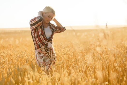 Woman in a wheat field on the background of the setting sun