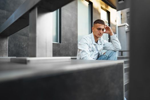 Young casual man sitting on stairs alone on city street