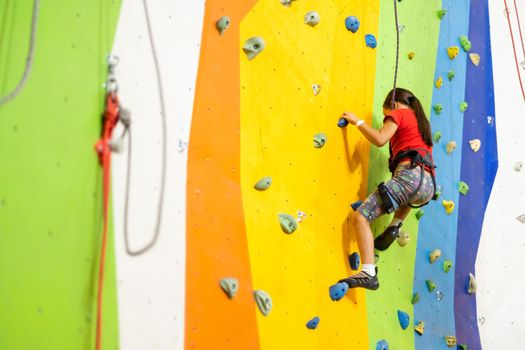 Sporty little girl climbing artificial boulder on practical wall in gym
