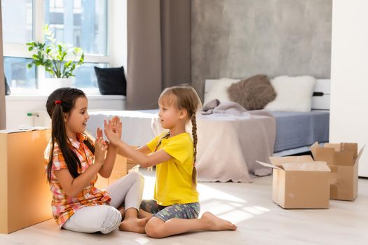 Happy family in living room. Preschool daughters sitting and help unpacking cardboard boxes belongings. Buy real estate, relocation at new modern house