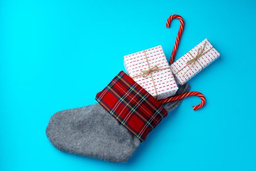 Christmas stocking with wrapped gifts and candy cane on blue background flat lay
