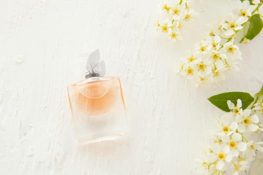 women's perfume in beautiful bottle and bird-cherry flowers on white background. Flat lay tools and accessories for woman