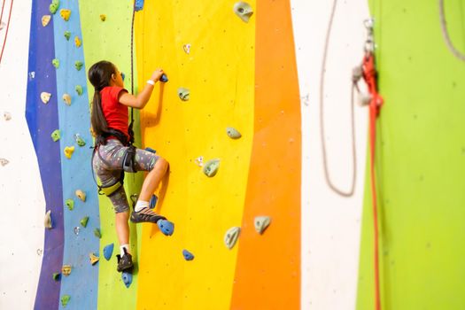 Sporty little girl climbing artificial boulder on practical wall in gym