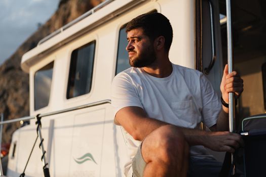 Portrait of a young caucasian bearded man sitting on a deck of sailboat, close up
