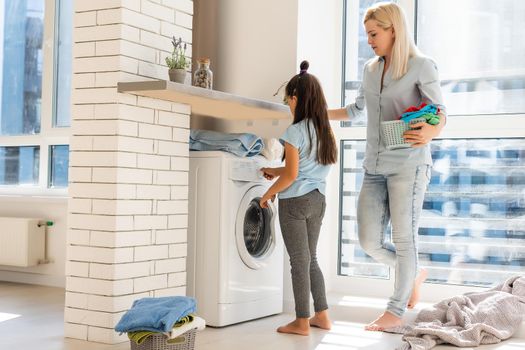 Young housewife and little girl doing laundry together