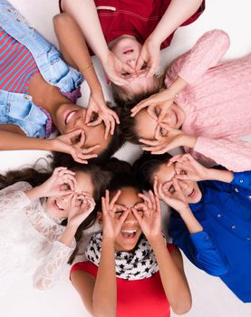 Kids lying on the floor head to head with glasses out of fingers