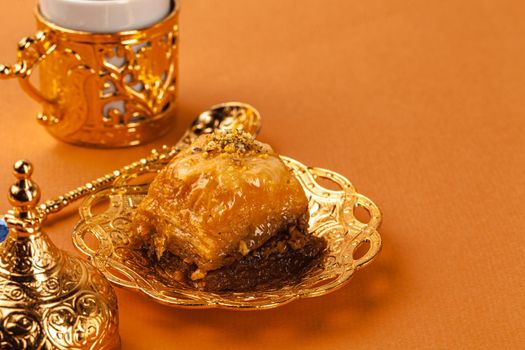Turkish dessert baklava served on traditional metal tableware on orange background