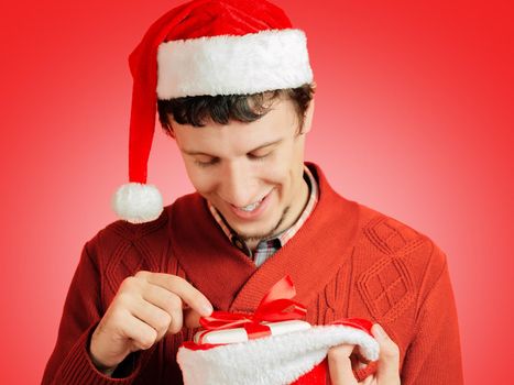 Young happy man is holding santa hat with gifts on a red background