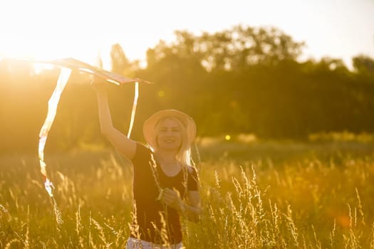 Happy young woman running with a kite on a glade at sunset in summer