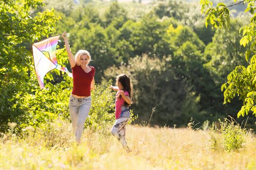 happy family mother and child run on meadow with a kite in the summer on the nature