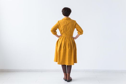 clothing, designer, people concept - back view of attractive woman in a yellow dress posing on white room