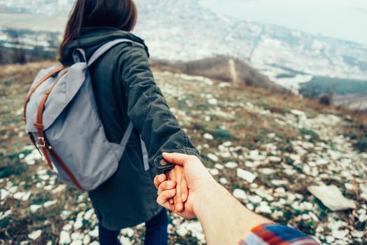 Hiker young woman holding man's hand and leading him on nature outdoor. Couple in love. Focus on hands. Image with instagram filter