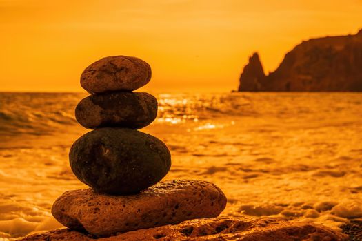 Balanced Pebbles Pyramid on the Beach on Sunny Day and Clear Sky at Sunset. Blue Sea on Background Selective focus, zen stones on sea beach, meditation, spa, harmony, calm, balance concept.