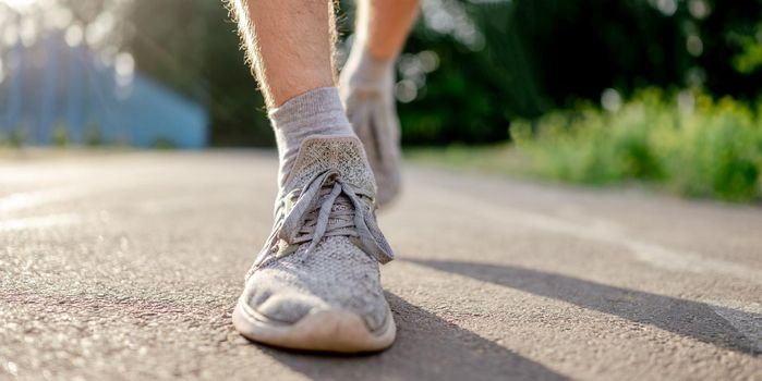 Closeup view of man guy legs feet wearing sport sneakers during running at the stadium road outdoors. Male person during morning workout. Sportsman exercising in summertime