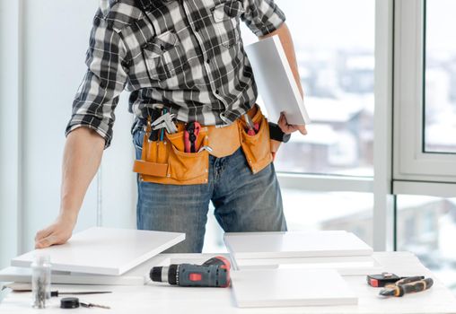 Man working connecting board of shelf during process of wooden furniture manufacturing in workshop