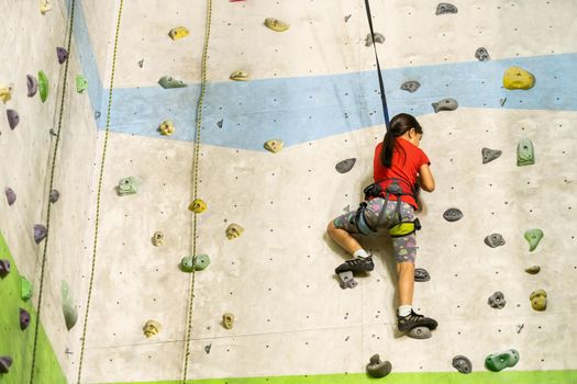 Sporty little girl climbing artificial boulder on practical wall in gym