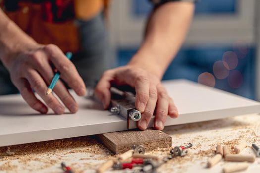 Man working with pencil marking holes during process of wooden furniture manufacturing in workshop