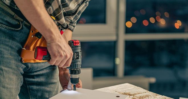 Man working making holes in board with drill during process of furniture manufacturing