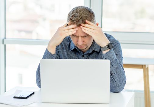 Puzzled businessman looking in laptop in light interior