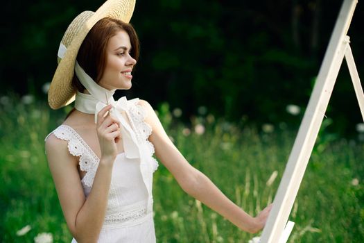 Woman in white dress paints a picture on nature easel. High quality photo