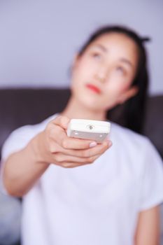 young woman holding a remote control air conditioner on sofa at home