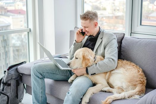 Handsome man cuddling lovely dog while working on sofa in bright room