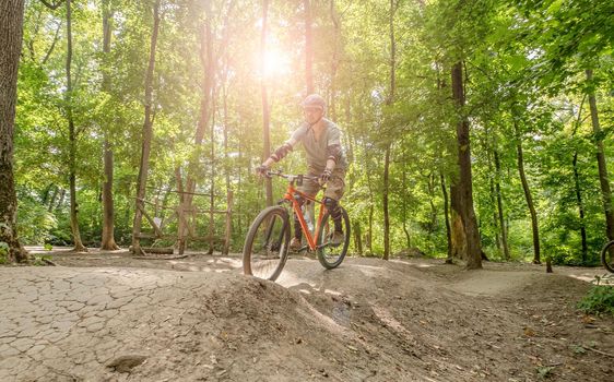 Man riding bicycle on forest road in shadows of high trees