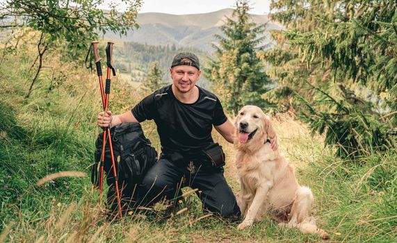 Man hiking in summer mountain with golden retriever dog