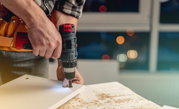 Man working with electric screwdriver and screws during process of furniture manufacturing