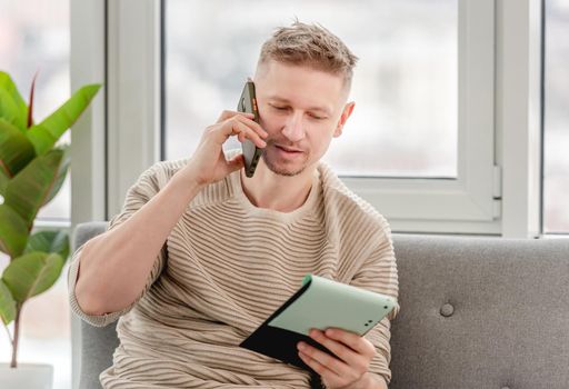 Man freelancer businessman talking by phone and holding notepad in his hands. Remote distance work at home during Covid pandemy