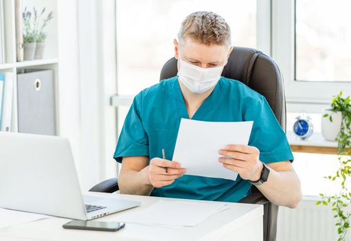 Doctor in face mask working on laptop in office