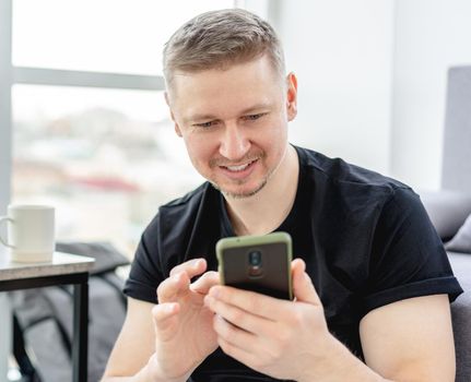 Smiling man looking into smart phone indoors