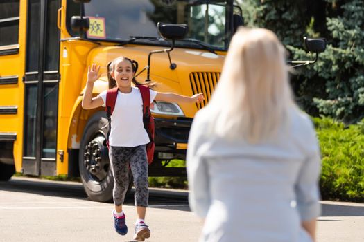 Kids student running into mother's hands to hug her after back to school near the school bus