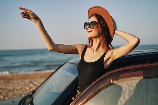 cheerful woman in sunglasses and a hat on the ocean near the car. High quality photo