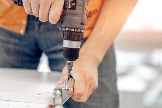 Man working making holes in board with drill during process of furniture manufacturing