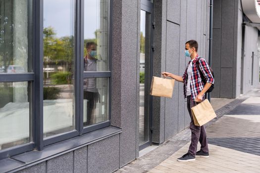 Delivery man holding paper bag with food, food delivery man in protective mask