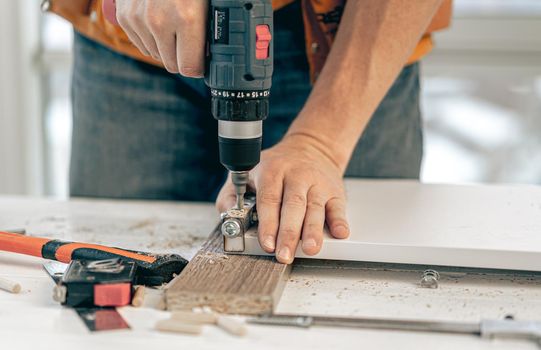 Man working using electric screwdriver during process of wooden furniture manufacturing in workshop