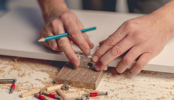 Man working using electric screwdriver during process of wooden furniture manufacturing in workshop