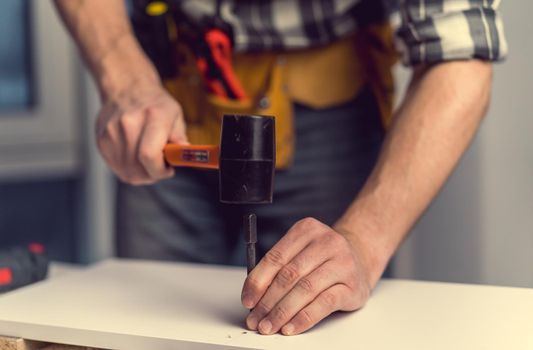 Man working with hammer and bit for hole during process of wooden furniture manufacturing in workshop