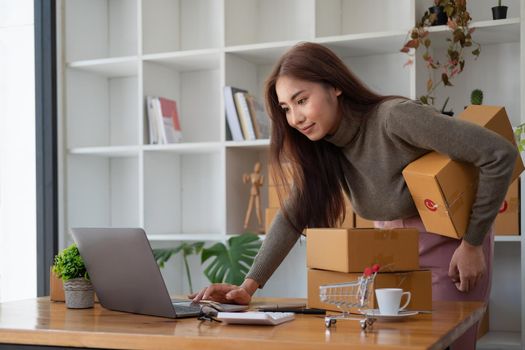 Starting Small business entrepreneur SME freelance,Portrait young woman working at home office, BOX,smartphone,laptop, online, marketing, packaging, delivery, SME, e-commerce concept