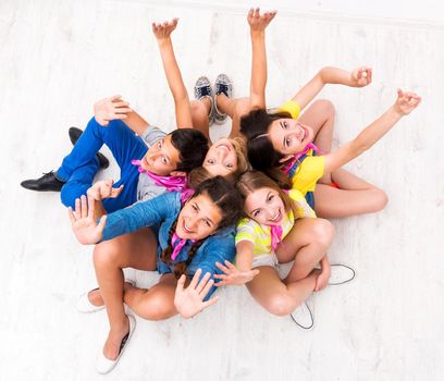 teenagers sitting on the floor with hands up smiling at camera, top view
