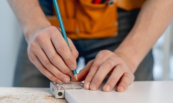 Man working with pencil marking holes during process of wooden furniture manufacturing in workshop